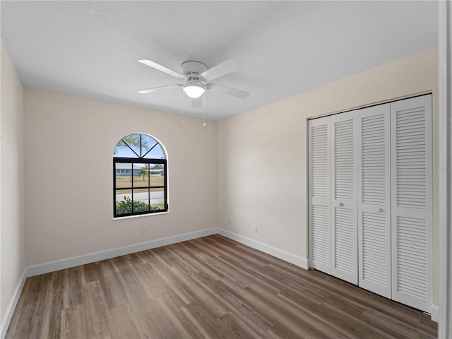 unfurnished bedroom featuring a closet, a ceiling fan, baseboards, and wood finished floors