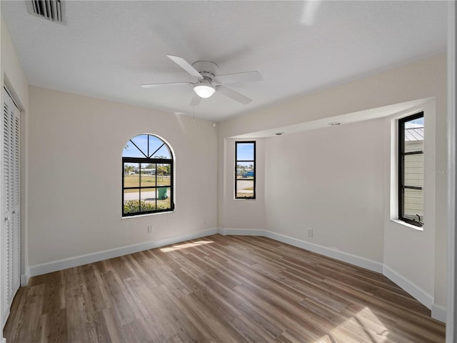 empty room featuring visible vents, a ceiling fan, baseboards, and wood finished floors