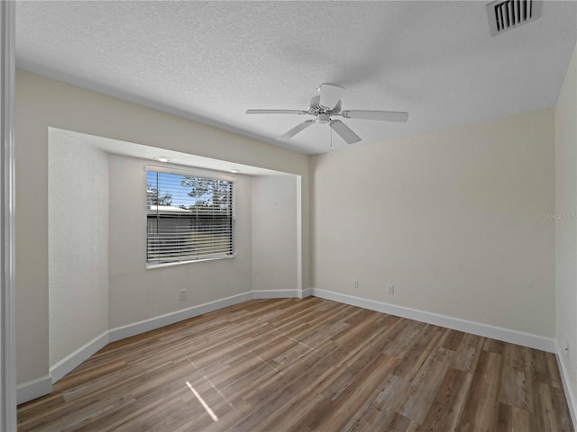 spare room featuring a textured ceiling, wood finished floors, visible vents, and baseboards