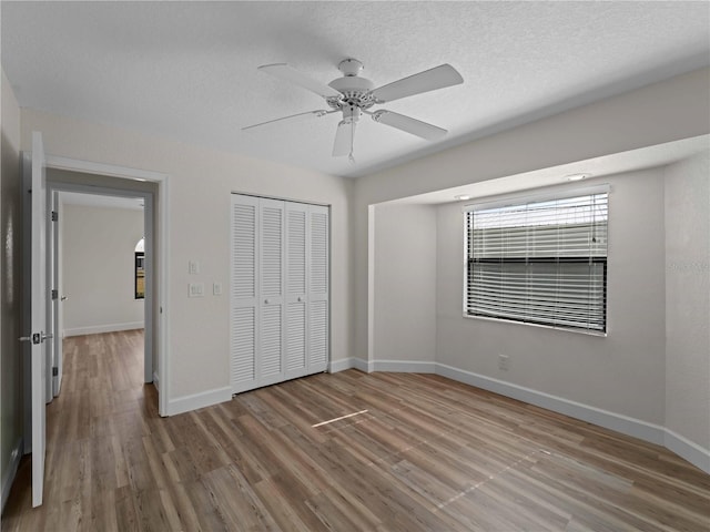 unfurnished bedroom featuring a closet, a textured ceiling, baseboards, and wood finished floors