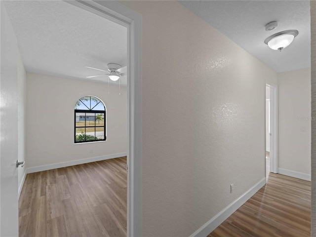 corridor featuring a textured wall, a textured ceiling, baseboards, and wood finished floors