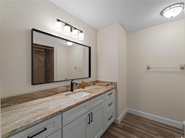 bathroom featuring vanity, wood finished floors, baseboards, a tile shower, and a textured ceiling