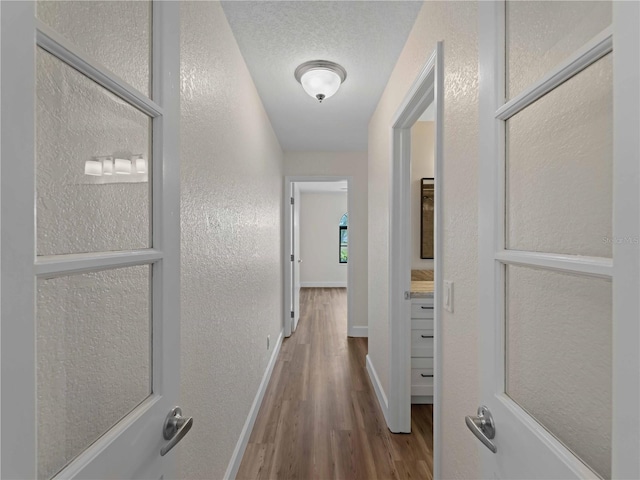 hall with baseboards, a textured ceiling, wood finished floors, and a textured wall