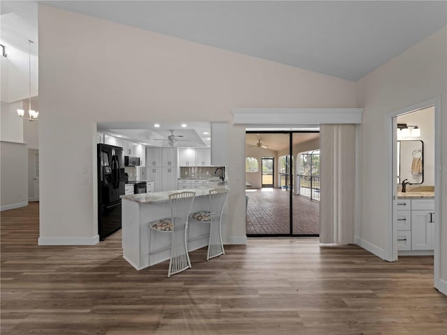 kitchen with wood finished floors, a peninsula, black appliances, and white cabinets