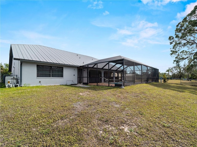 rear view of property with stucco siding, metal roof, glass enclosure, and a yard