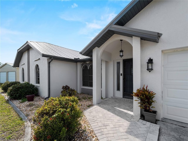 view of exterior entry featuring a standing seam roof, metal roof, a garage, and stucco siding