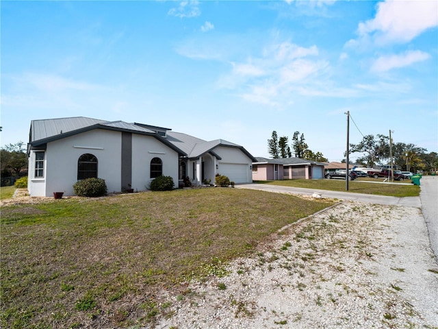 view of front of house featuring a front lawn, stucco siding, metal roof, a garage, and driveway