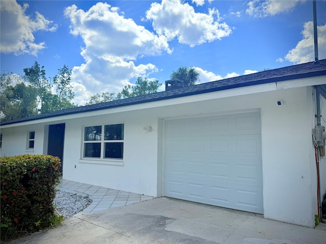 view of front facade with stucco siding, roof with shingles, concrete driveway, and an attached garage