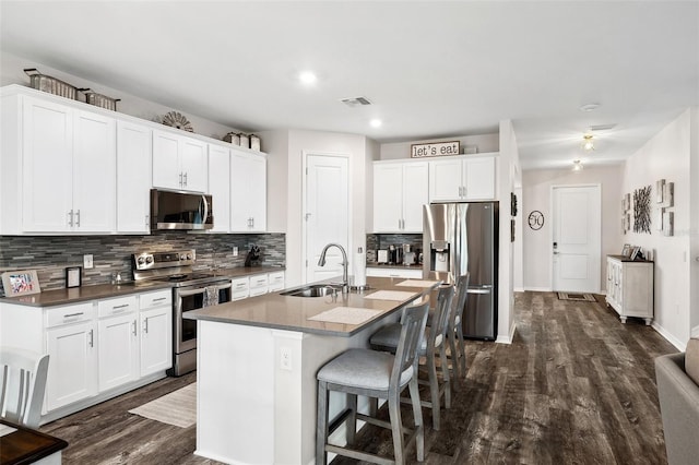 kitchen with visible vents, a kitchen bar, a center island with sink, a sink, and appliances with stainless steel finishes