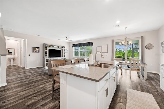 kitchen featuring a breakfast bar, ceiling fan with notable chandelier, a sink, dark wood finished floors, and white cabinetry