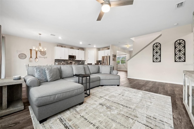 living room with visible vents, ceiling fan with notable chandelier, dark wood-type flooring, and baseboards