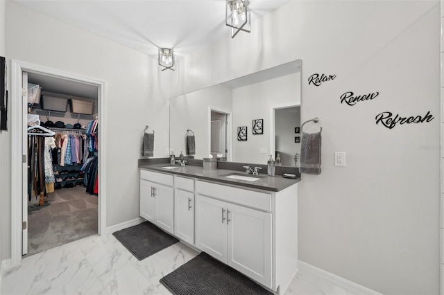 full bath featuring double vanity, marble finish floor, a spacious closet, and a sink