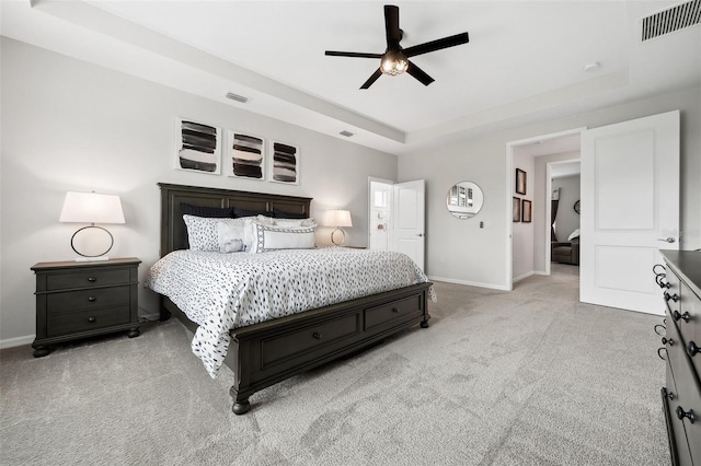 carpeted bedroom with a tray ceiling, baseboards, visible vents, and ceiling fan