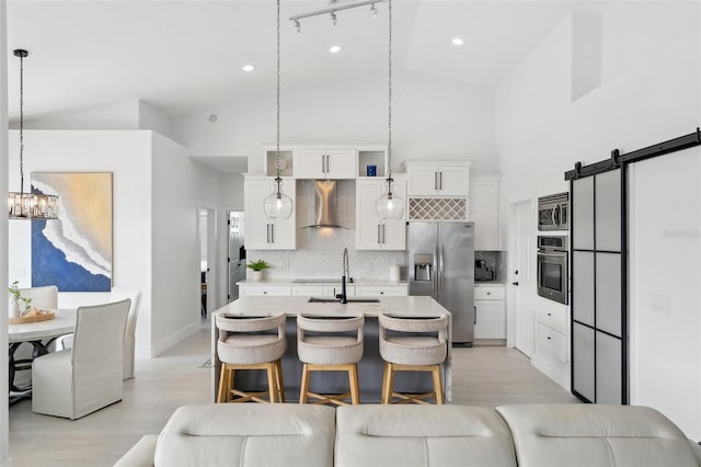 kitchen with light countertops, a barn door, stainless steel appliances, wall chimney exhaust hood, and a sink