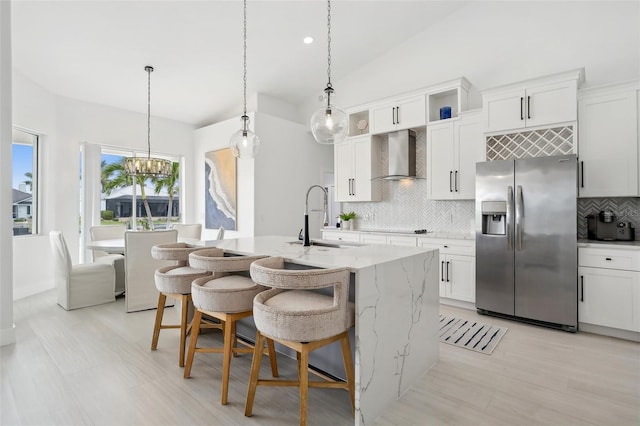 kitchen with wall chimney range hood, a kitchen bar, vaulted ceiling, stainless steel refrigerator with ice dispenser, and a sink