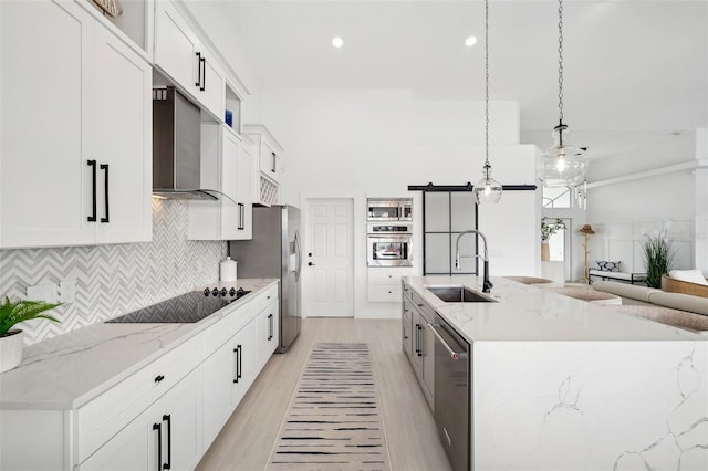 kitchen featuring a center island with sink, stainless steel appliances, a sink, white cabinetry, and wall chimney exhaust hood