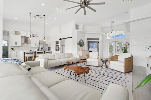 living area with visible vents, high vaulted ceiling, a ceiling fan, a barn door, and french doors