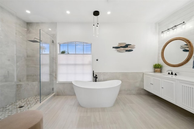 bathroom featuring a freestanding tub, a walk in shower, recessed lighting, tile walls, and vanity