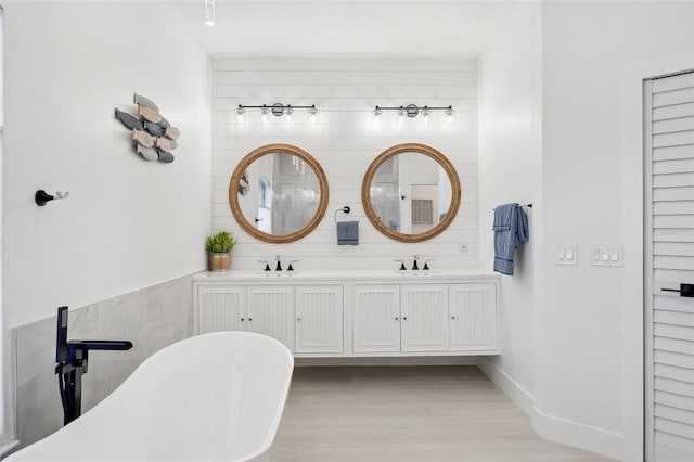 bathroom with double vanity, a sink, wood finished floors, and a freestanding tub