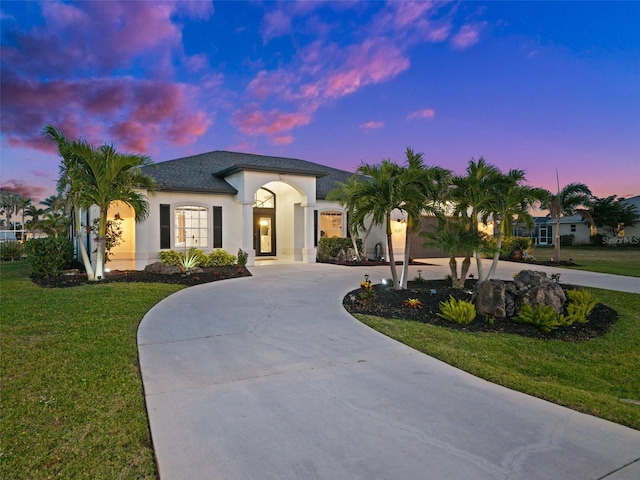 view of front of property with curved driveway, french doors, a yard, and stucco siding