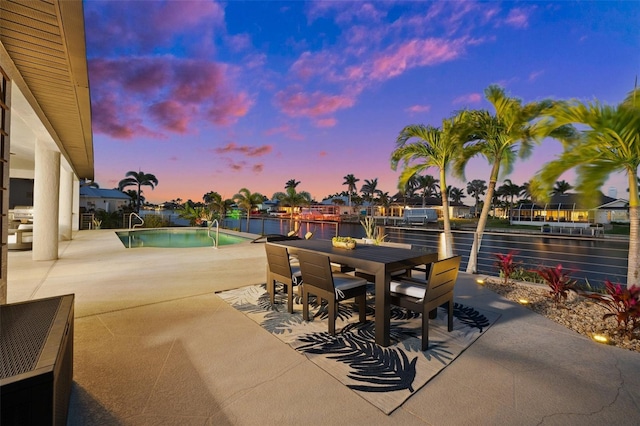 patio terrace at dusk featuring an outdoor pool, outdoor dining area, and a water view