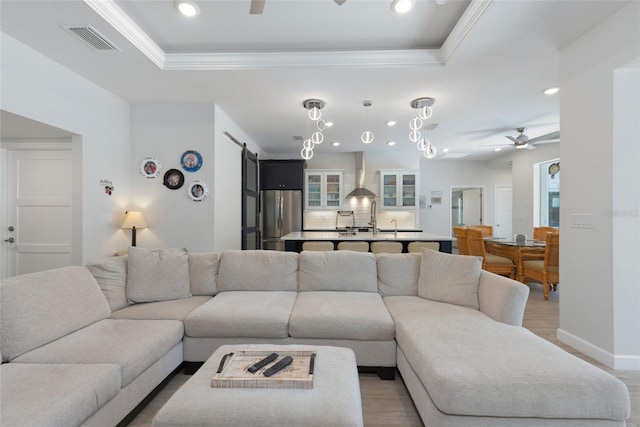 living room with a ceiling fan, visible vents, crown molding, a barn door, and a raised ceiling