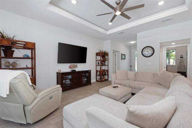 living room with a raised ceiling, visible vents, light wood-type flooring, and ornamental molding