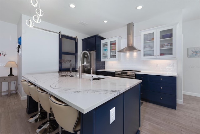 kitchen with backsplash, a barn door, exhaust hood, stainless steel appliances, and blue cabinets