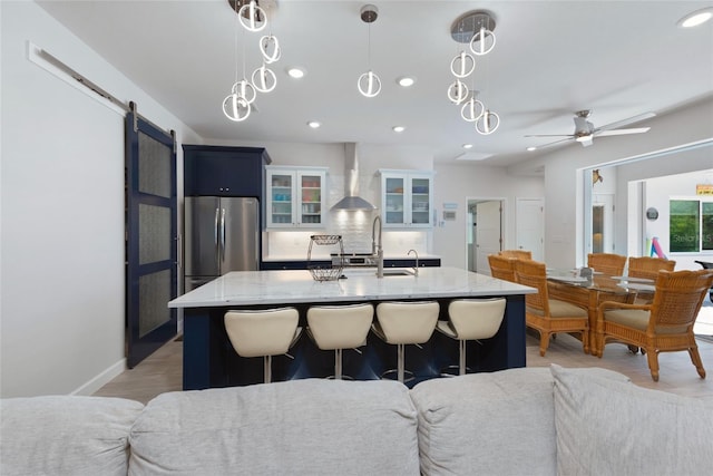 kitchen with wall chimney range hood, a barn door, open floor plan, and freestanding refrigerator