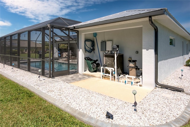 back of property with stucco siding, a patio, glass enclosure, an outdoor pool, and metal roof