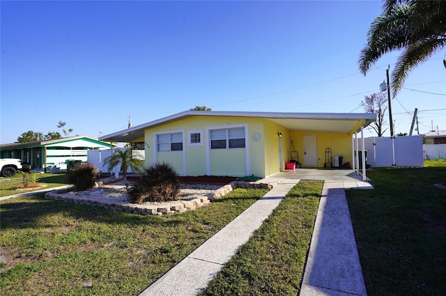 view of front of house with an attached carport, fence, a front yard, stucco siding, and driveway