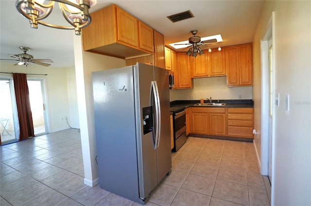 kitchen with light tile patterned floors, a ceiling fan, a sink, appliances with stainless steel finishes, and dark countertops