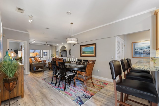 dining area featuring light wood-style flooring, arched walkways, visible vents, and ornamental molding