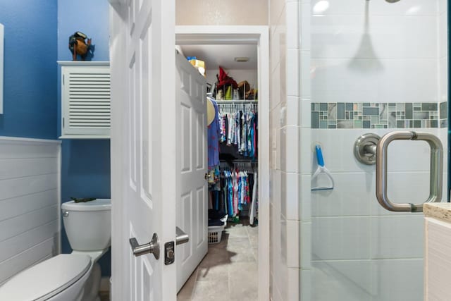 bathroom featuring a wainscoted wall, a spacious closet, toilet, and a stall shower