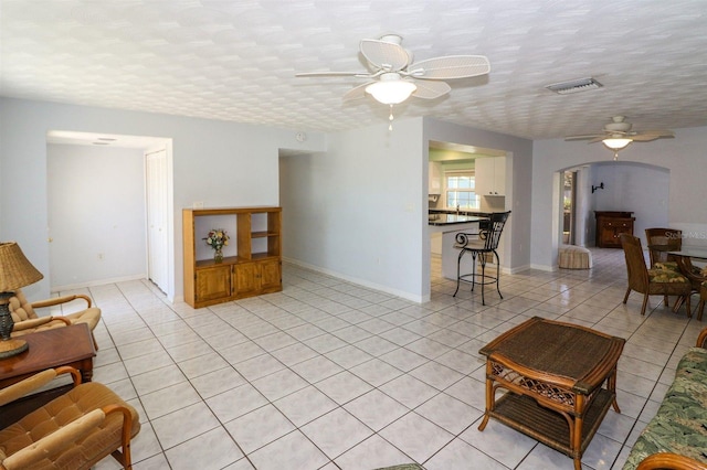 living room with visible vents, a textured ceiling, arched walkways, light tile patterned flooring, and ceiling fan