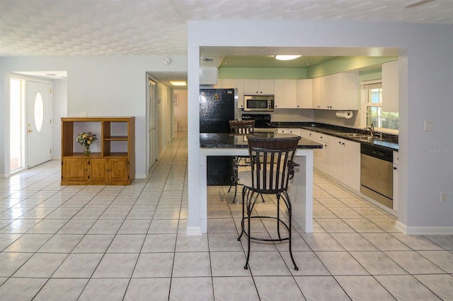 kitchen featuring a sink, dark countertops, appliances with stainless steel finishes, and light tile patterned flooring