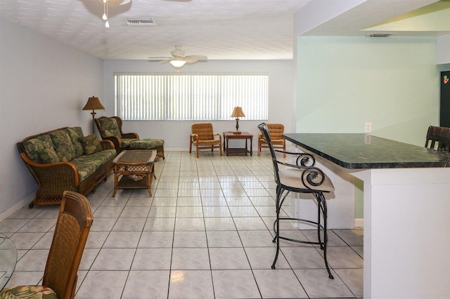 living area featuring light tile patterned floors, visible vents, baseboards, and ceiling fan