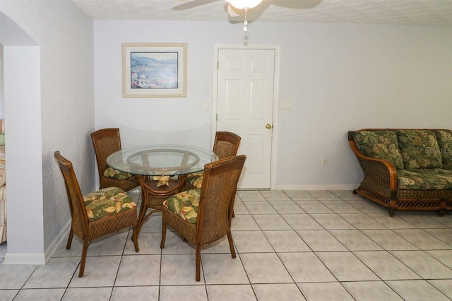 dining space featuring light tile patterned floors, baseboards, arched walkways, and a ceiling fan