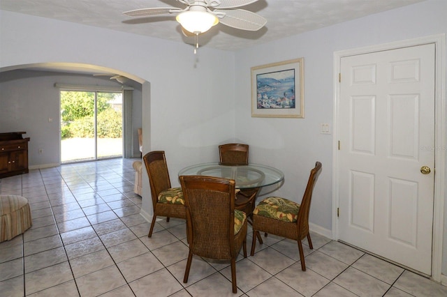 dining room with light tile patterned flooring, baseboards, arched walkways, and ceiling fan