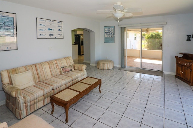 living area featuring light tile patterned floors, a ceiling fan, arched walkways, and baseboards