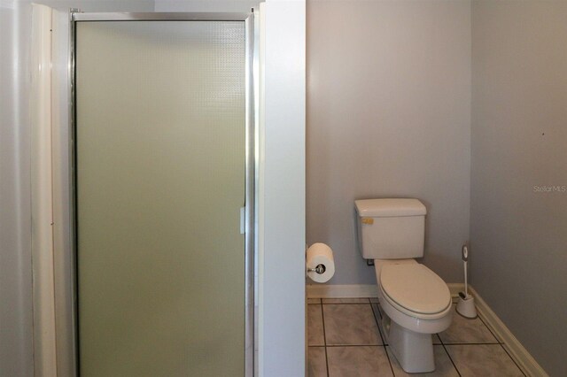 full bath featuring tile patterned floors, toilet, baseboards, and a shower stall