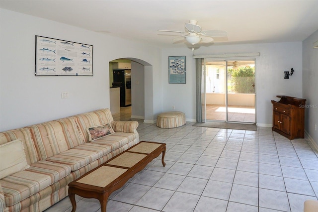 living area with light tile patterned flooring, arched walkways, baseboards, and a ceiling fan