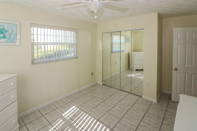 unfurnished bedroom featuring light tile patterned flooring, baseboards, a closet, and ceiling fan