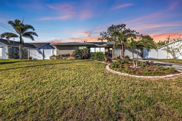 view of front of property with fence, driveway, solar panels, an attached garage, and a front lawn