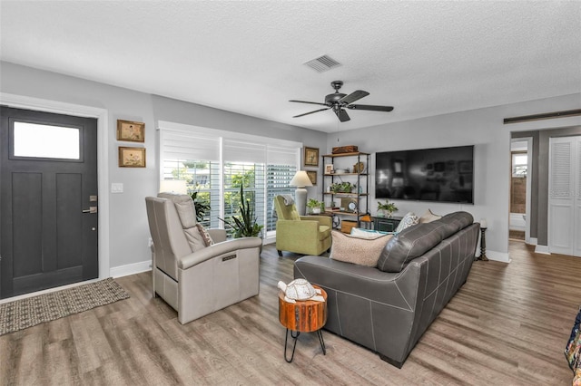 living room featuring visible vents, light wood-style flooring, a textured ceiling, and a ceiling fan