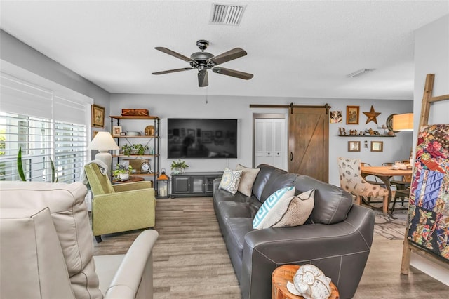 living area with a barn door, visible vents, a ceiling fan, and wood finished floors