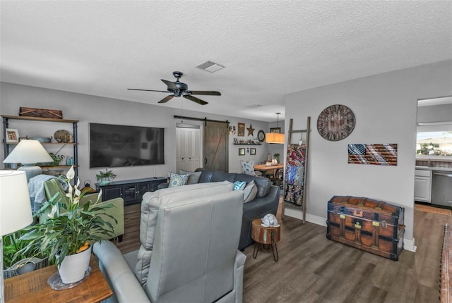 living room with visible vents, a textured ceiling, wood finished floors, a barn door, and ceiling fan