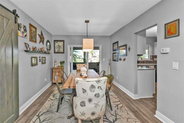 dining area with a barn door, a textured ceiling, baseboards, and wood finished floors