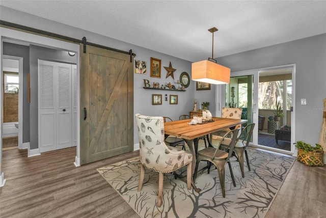 dining space featuring a textured ceiling, baseboards, a barn door, and wood finished floors