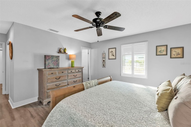 bedroom with a ceiling fan, wood finished floors, visible vents, baseboards, and a textured ceiling